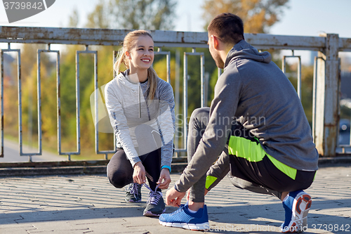 Image of smiling couple tying shoelaces outdoors