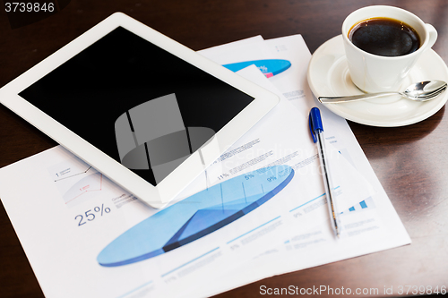 Image of close up of tablet pc, charts and coffee on table