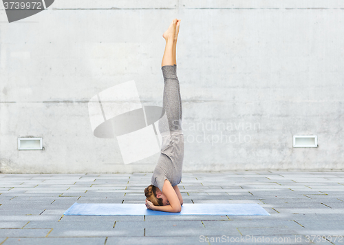 Image of woman making yoga in headstand pose on mat