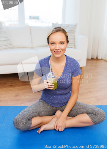 Image of happy woman with smoothie sitting on mat at home