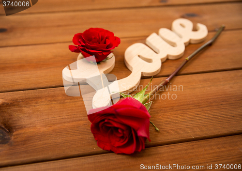 Image of close up of word love cutout with red rose on wood