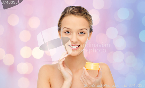 Image of happy young woman applying cream to her face