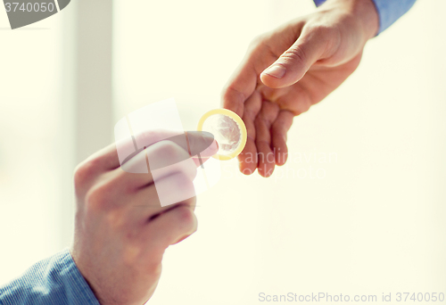 Image of close up of male gay couple hands giving condom