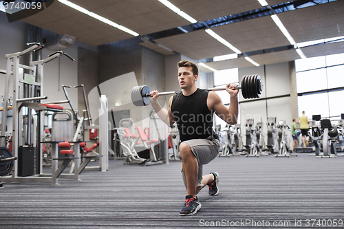 Image of young man flexing muscles with barbell in gym