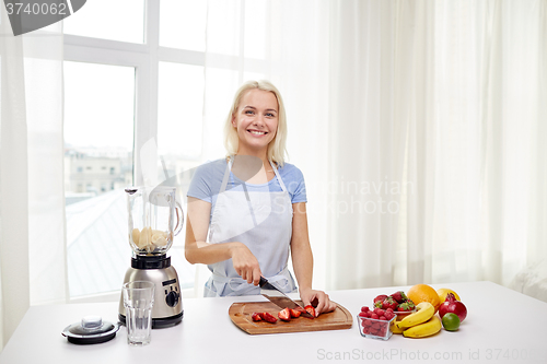 Image of smiling woman with blender preparing shake at home