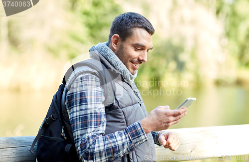 Image of happy man with backpack and smartphone outdoors