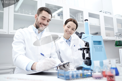 Image of scientists with clipboard and microscope in lab