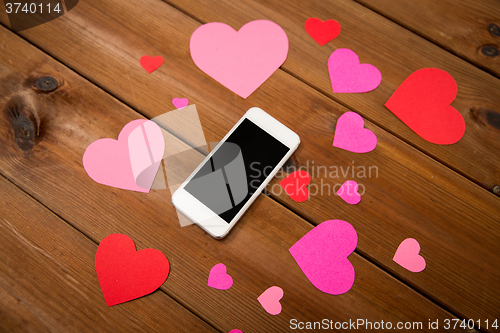 Image of close up of smartphone and hearts on wood