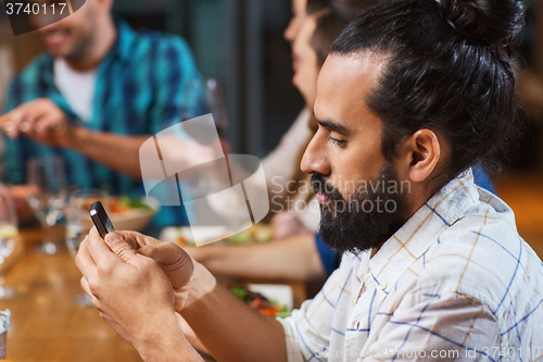Image of man with smartphone and friends at restaurant