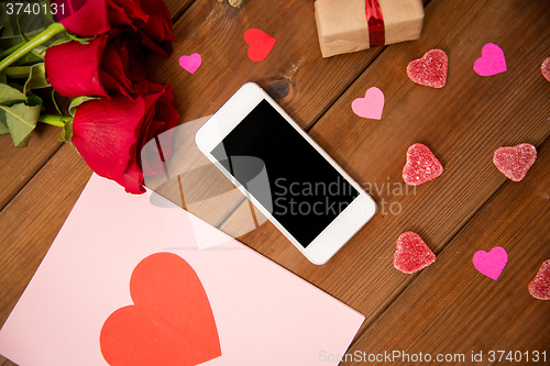 Image of close up of smartphone, gift, red roses and hearts