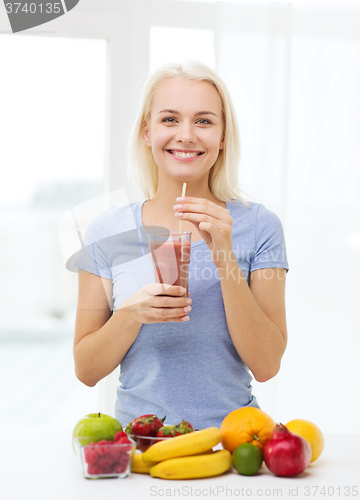 Image of smiling woman drinking fruit shake at home