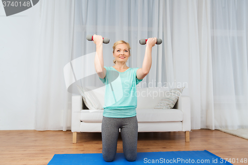 Image of woman exercising with dumbbells on mat at home