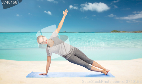 Image of woman making yoga in side plank pose on beach 