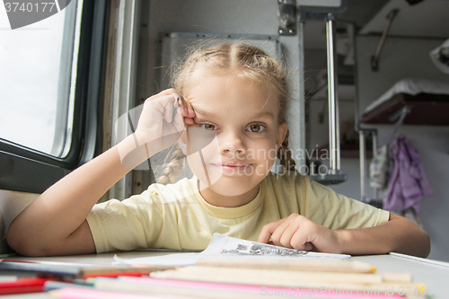 Image of Girl happily looks into the frame, drawing pencils in a train