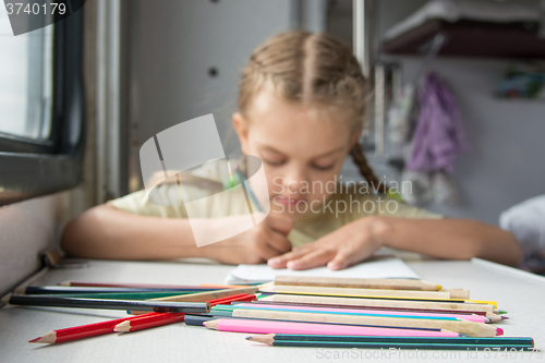 Image of  Pencils in the foreground, in the background a six year old girl drawing pencils in a second-class train carriage