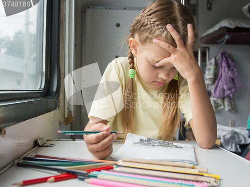 Image of Six year old girl thoughtfully draws pencils in second-class train carriage