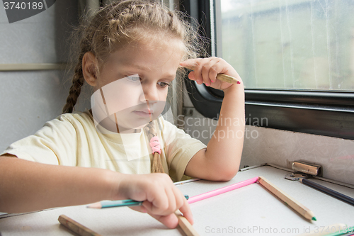 Image of Four-year girl playing with pencils reserved seats at a table in a train