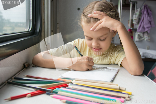 Image of Six-year girl joyfully draws pencils in second-class train carriage