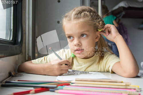 Image of Six year old girl lost in thought looked out the window drawing pencils in second-class train carriage