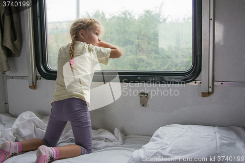 Image of Four-year girl on the side of the shelf of the train looking out the window