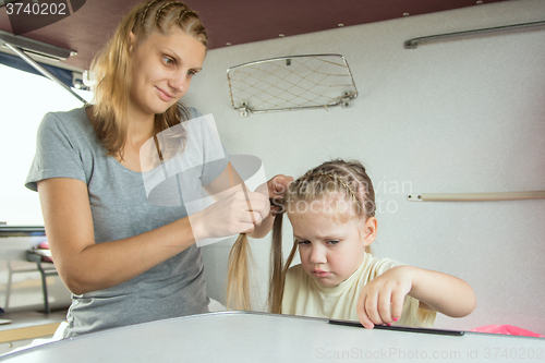 Image of The girl is sick mother braids her pigtails, on a cot in a train