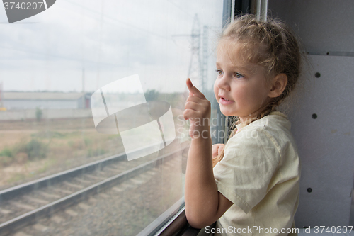 Image of  Four-year girl shows a finger on something from the window of a train car