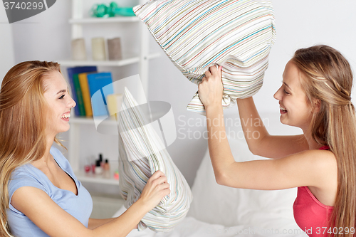 Image of happy teen girl friends fighting pillows at home