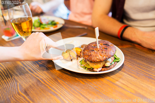 Image of close up of friends hands sharing burger at bar