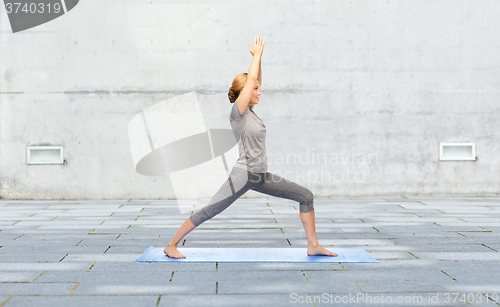 Image of woman making yoga warrior pose on mat outdoors