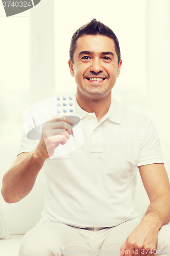 Image of happy man showing pack of pills at home