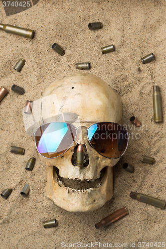 Image of skull lying in the sand, scattered rifle and pistol cartridges. concept of war