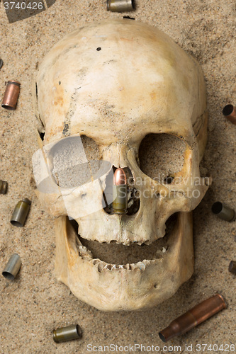 Image of skull lying in the sand, scattered rifle and pistol cartridges. concept of war