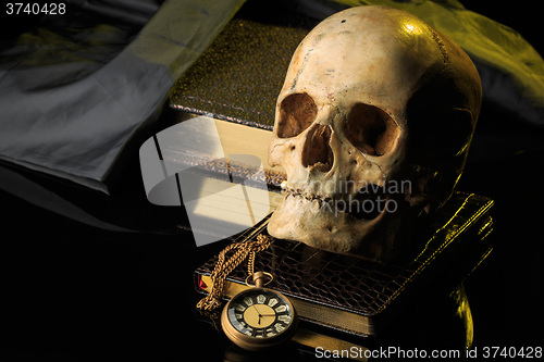 Image of human skull on a book next to the clock. concept of black magic