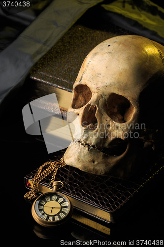 Image of human skull on a book next to the clock. concept of black magic