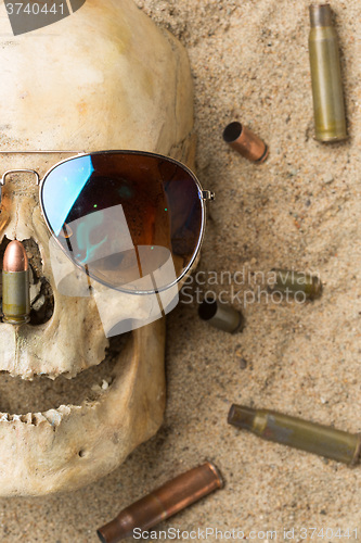 Image of skull lying in the sand, scattered rifle and pistol cartridges. concept of war