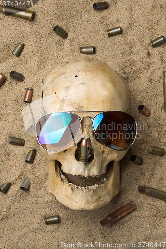 Image of skull lying in the sand, scattered rifle and pistol cartridges. concept of war