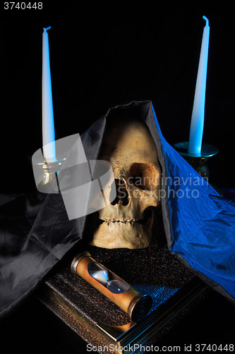 Image of human skull on a book next to the clock. concept of black magic