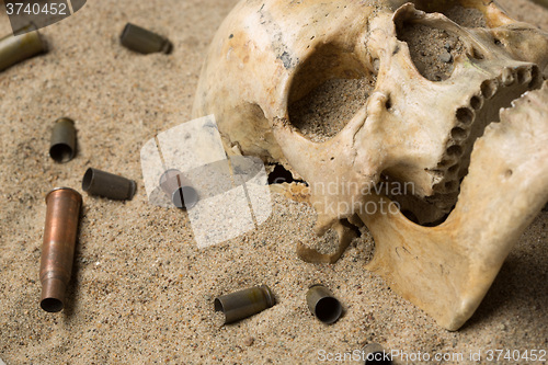 Image of skull lying in the sand, scattered rifle and pistol cartridges. concept of war