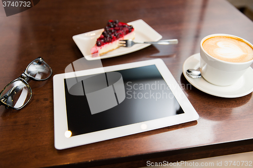Image of close up of tablet pc, coffee cup and cake
