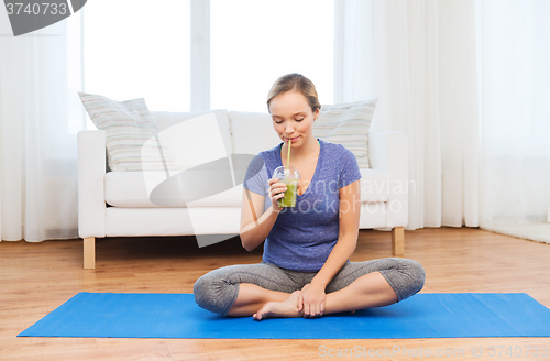 Image of happy woman with smoothie sitting on mat at home
