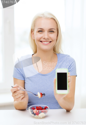 Image of woman with smartphone eating fruits at home