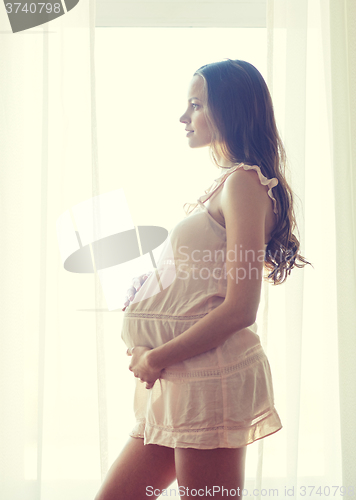 Image of happy pregnant woman near window at home