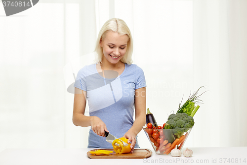 Image of smiling young woman chopping vegetables at home