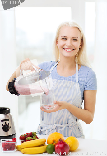 Image of smiling woman with blender preparing shake at home