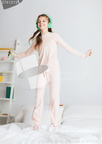 Image of girl jumping on bed with smartphone and headphones