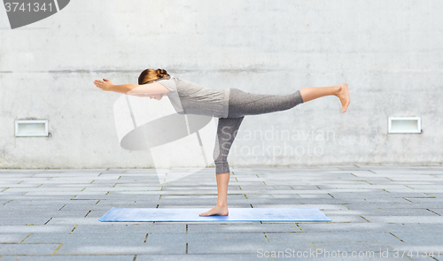 Image of woman making yoga warrior pose on mat outdoors