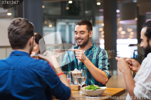 Image of happy friends taking picture of food at restaurant