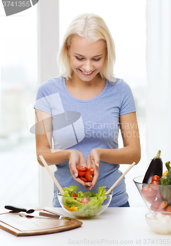 Image of smiling woman cooking vegetable salad at home