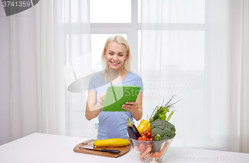 Image of smiling young woman with tablet pc cooking at home