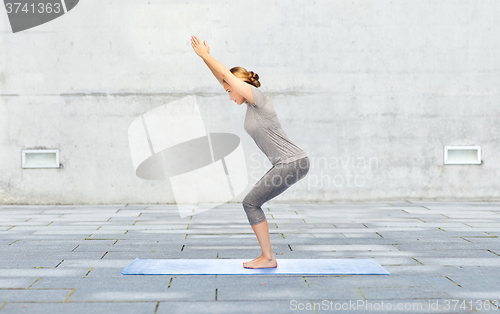 Image of woman making yoga in chair pose on mat outdoors